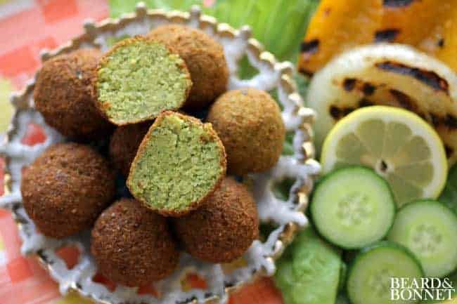 A small dish of falafel next to a plate of grilled vegetables. 