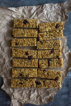 A crumpled piece of brown butcher paper on top of a metal table top. A large pan of granola bars has been cut into 14 equal rectangles and placed back together into the shape of the pan.