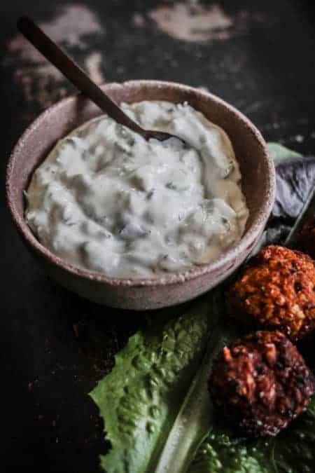 A bowl of homemade tzatziki dip next to a platter of sweet potato falafel