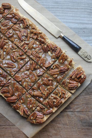 Pecan bars on parchment paper with a knife next to them