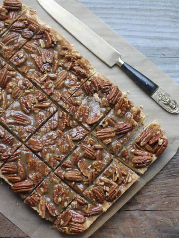 Pecan bars on parchment paper with a knife next to them