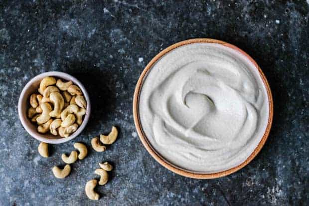 A bowl of raw cashews next to a bowl of creamy cashew cream