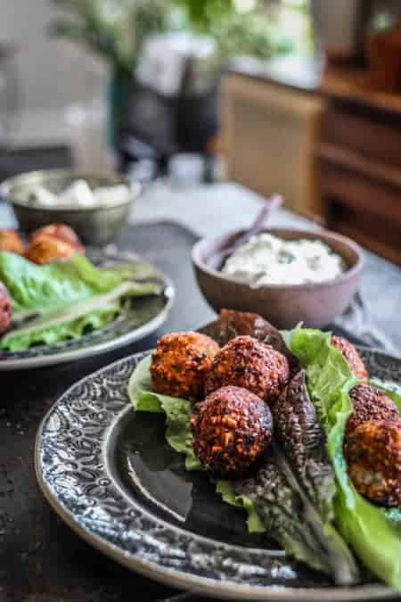 2 plates on a table with falafel and lettuce wrap ingredients on them