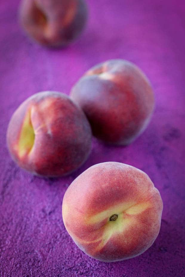 3 ripe peaches sitting on top of a magenta colored background