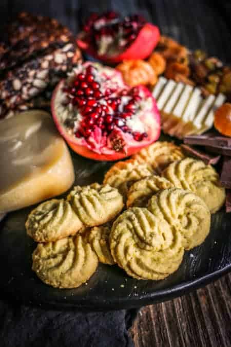 A dessert inspired cheeseboard with Gluten Free Italian Polenta Cookies, cheeses, fresh pomegranate, pan forte wedges, dried fruits, and nuts