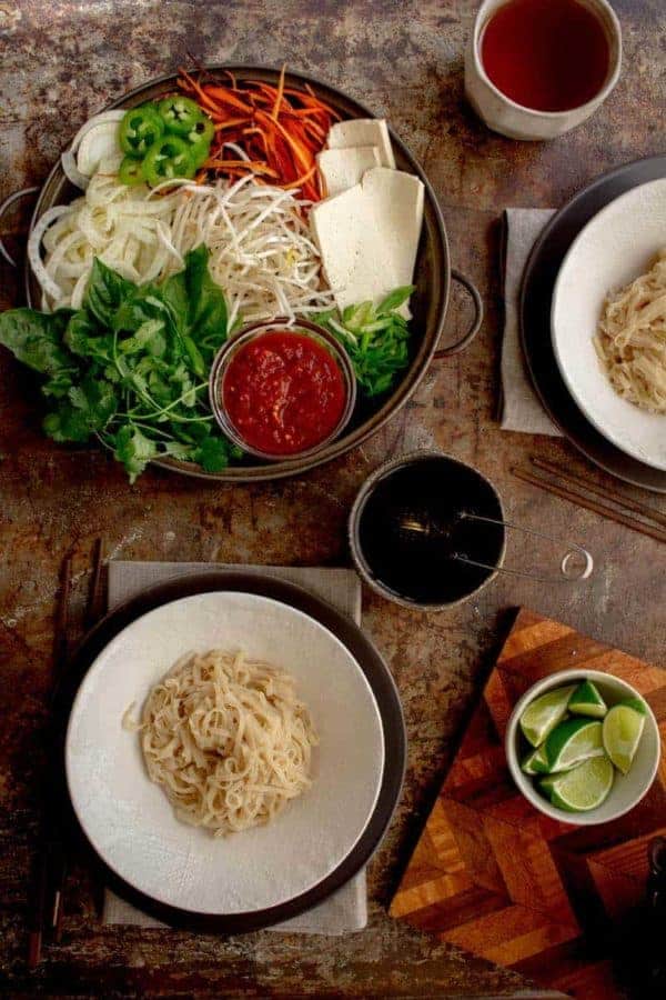 A table set up of pho noodles in bowls and all of the toppings on platters around them for building a bowl of pho
