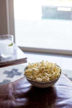 A big bowl of popcorn is sitting on an ottoman