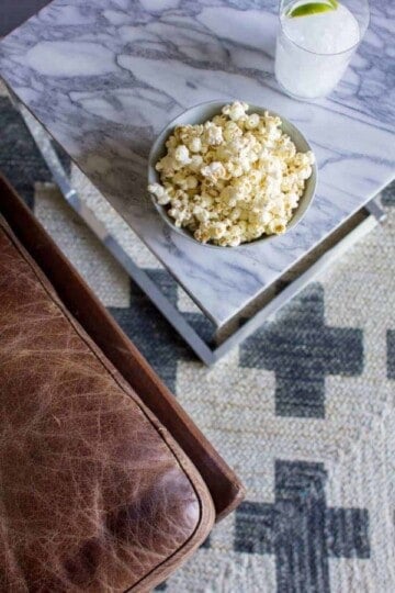 Cacio e Pepe Popcorn in a bowl on a marble coffee table next to a letter couch