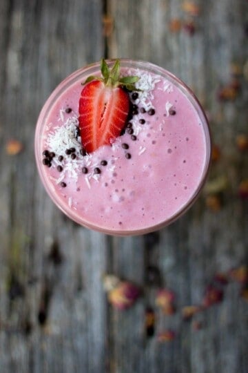 looking down into a glass that is full of a pink smoothie that has chocolate covered chia seeds, shredded coconut, and half of a beautiful strawberry on top.