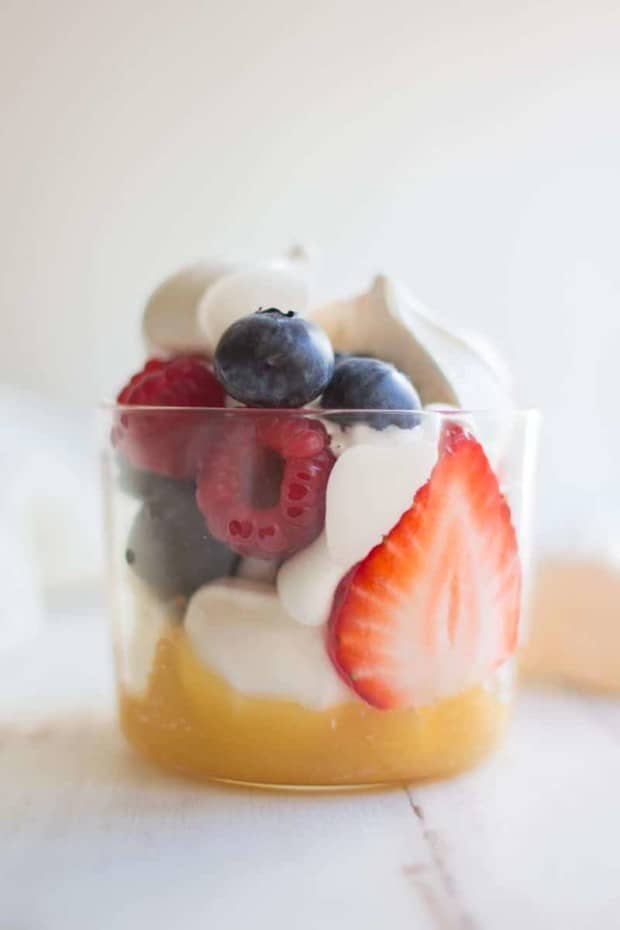a clear glass with lemon curd in the bottom, miniature store bought meringues, whipped cream, and fresh berries