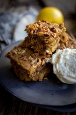 Three apple brown butter blondies are stacked on a black plate, 2 on the bottom and 1 on top, there is a scoop of vanilla ice cream next to the blondies