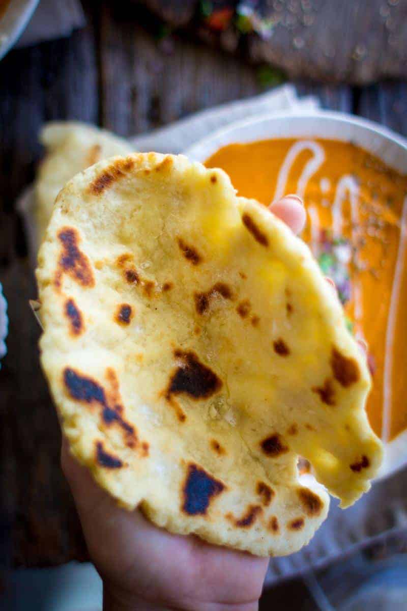 A piece of Gluten Free Roasted Garlic Naan being held to show it is large, about the size of a woman's hand. 