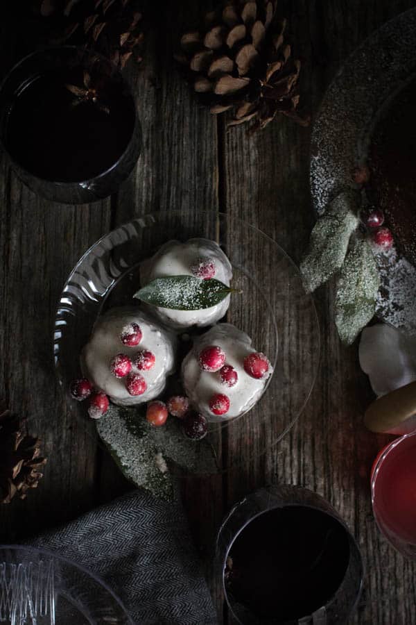 top down image of 3 small cupcakes drizzled in eggnog icing and topped with sugared cranberries and bay leaves. 