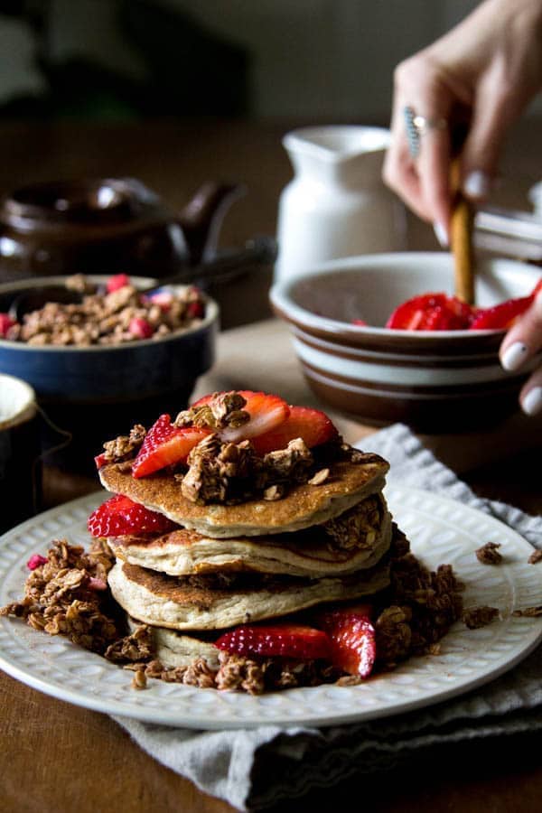 stack of pancakes with chocolate granola sprinkled over top and in batter, and strawberries