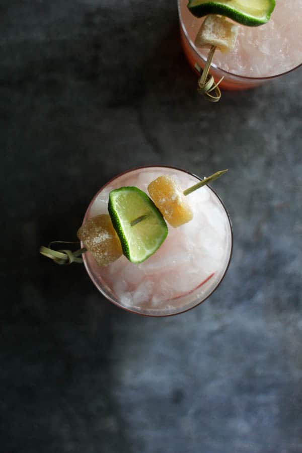 Top down photograph of two glasses of Rhubarb Ginger Beer Margaritas. There are skewers of candied ginger and lime wheels garnishing each glass