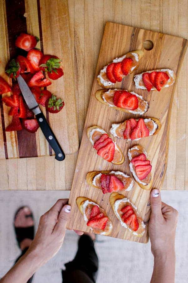 Pieces of Rhubarb Jam & Vanilla Scented Goat Cheese Crostini topped with freshly sliced strawberries and cracked black pepper on a serving board