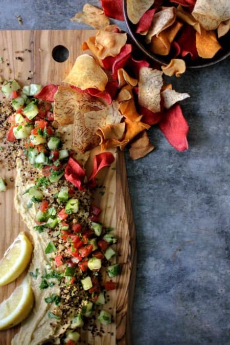 A Deconstructed Tabbouleh Hummus Platter, hummus on the bottom topped with crispy quinoa, cucumbers, tomatoes, and herbs. Served with root vegetable chips