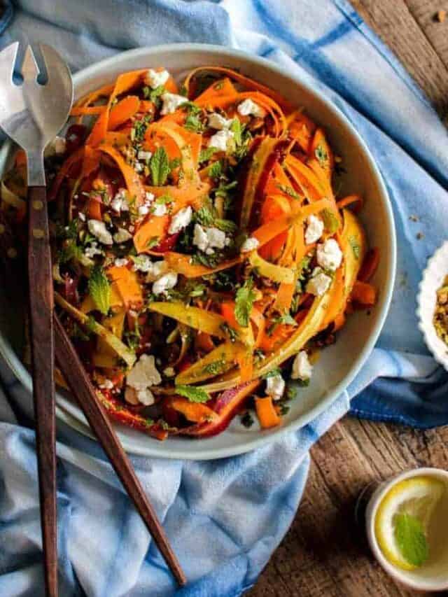 Carrot, Feta, and Pistachio Salad with Orange Blossom Toss dressing is on a table in a large serving bowl with utensils