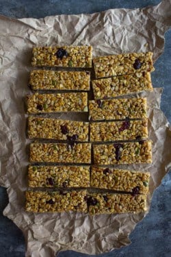 14 rectangular granola bars sit on a piece of crumpled parchment ob a metal table top