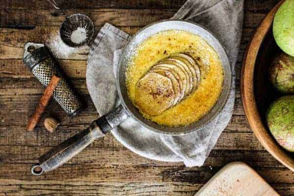 Baked apple custard on table with sliced fresh apples and cinnamon sticks