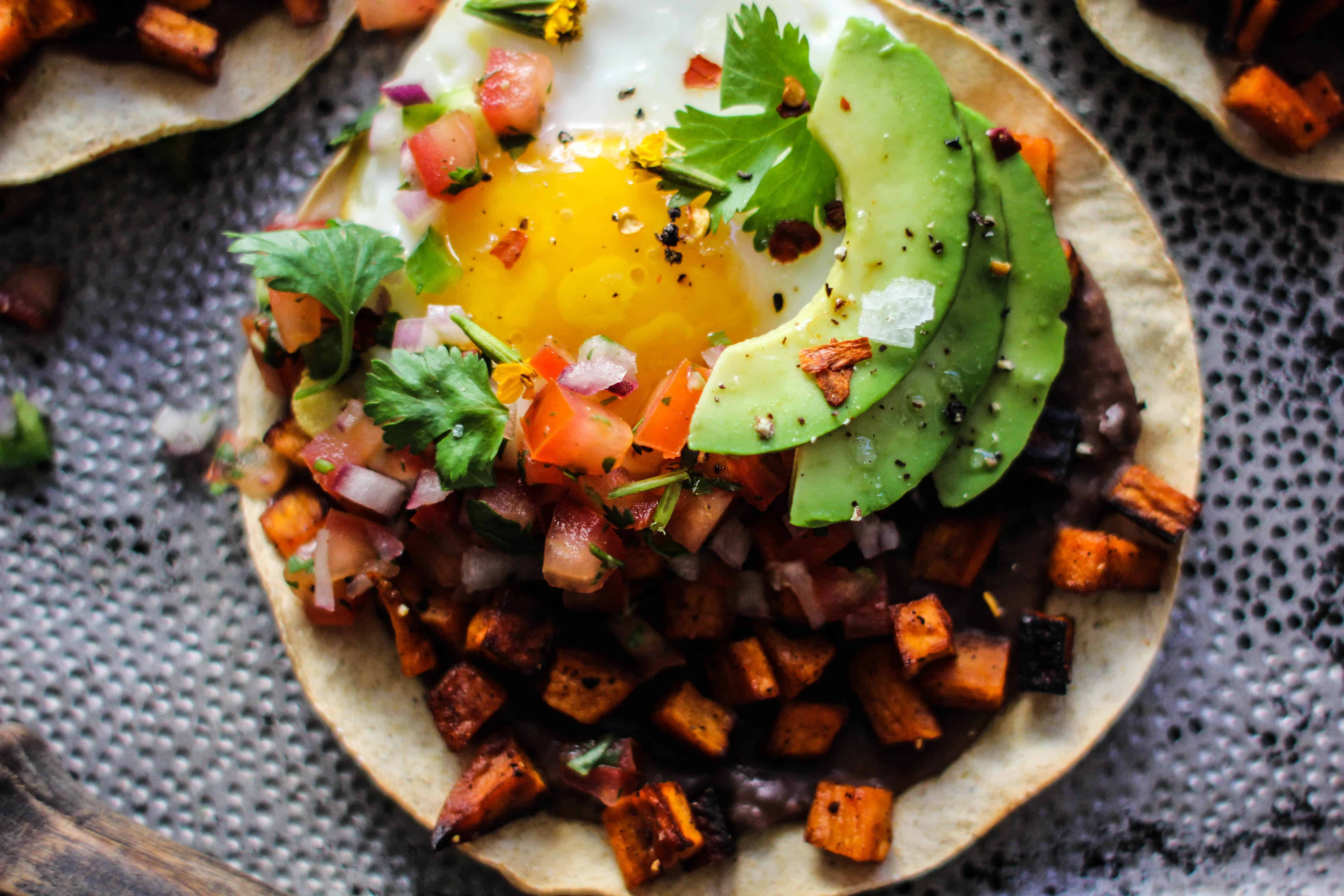 tostada with refried black beans, roasted sweet potatoes, fried egg, and avocado