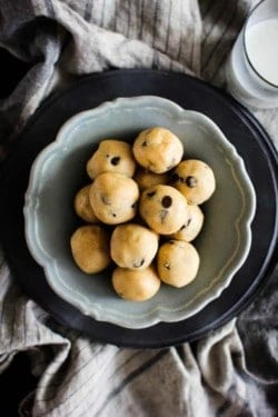 A small blue bowl sits inside of a brown bowl on top of linen napkins. The blue bowl is filled with round chocolate chip cookie dough bites