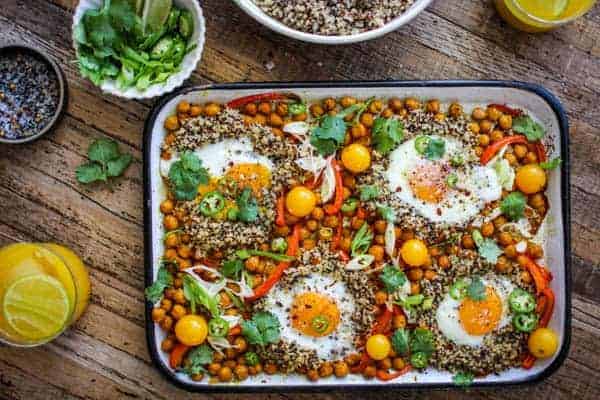 Sheet pan full of roasted chickpeas, red bell pepper, and cherry tomatoes with quinoa an perfectly baked sunny side up eggs.