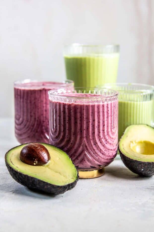 4 glasses on a white background. 2 have a pruple smoothie and 2 have a green smoothie