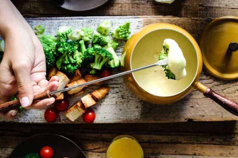 Broccoli being dipped into cheese fondue