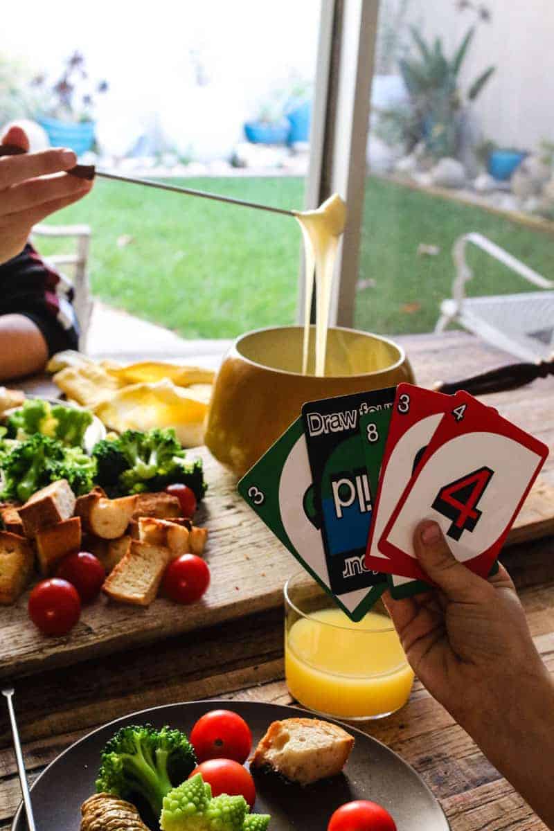 Kids playing Uno, fondue cheese board, girl dipping bread into fondue