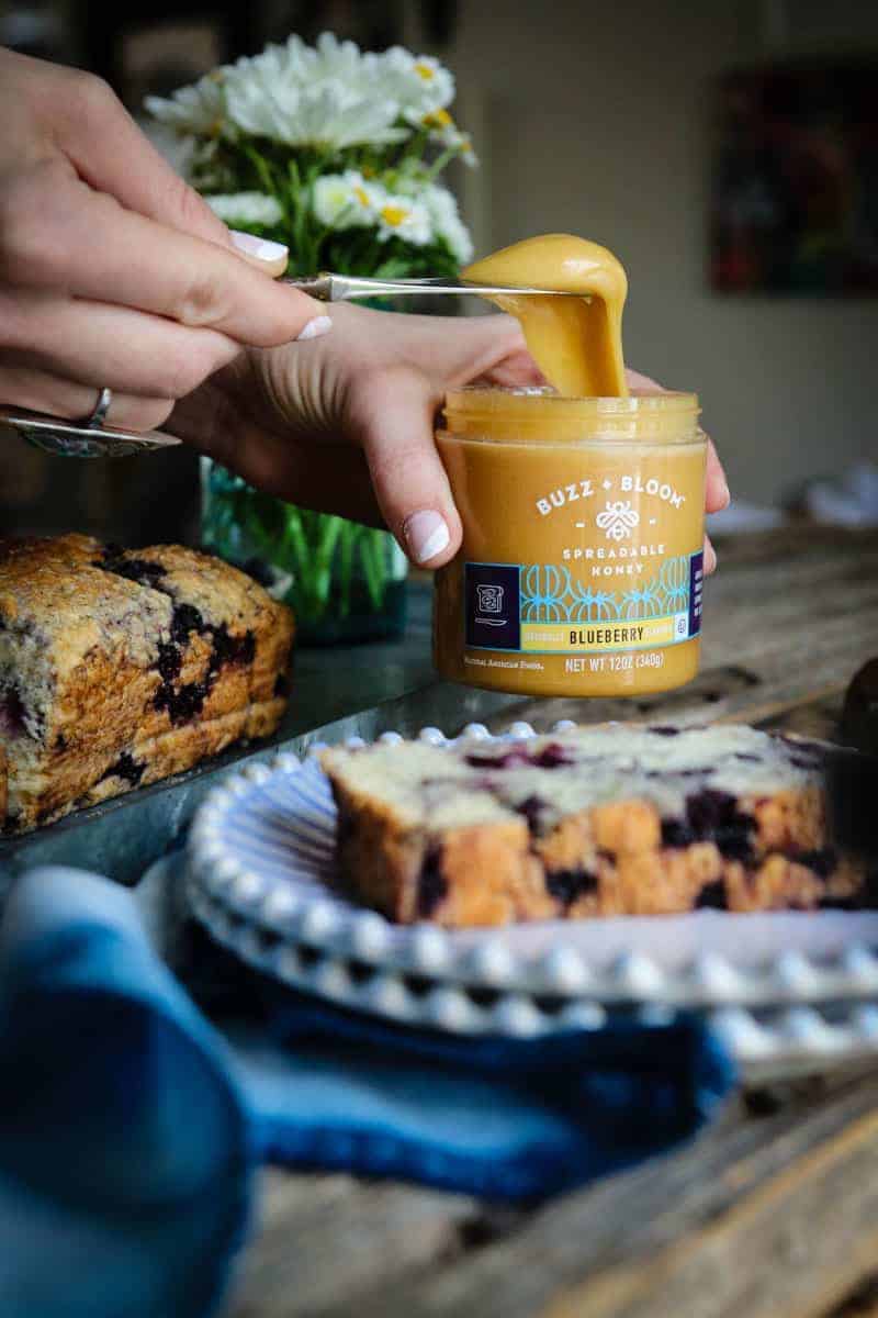 A slice of blueberry honey quick bread and blueberry spreadable honey being scooped from the jar