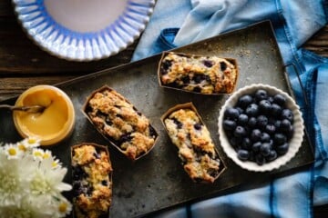 blueberry quick bread mini loaves on tray with fresh blueberries, spreadable honey, and flowers