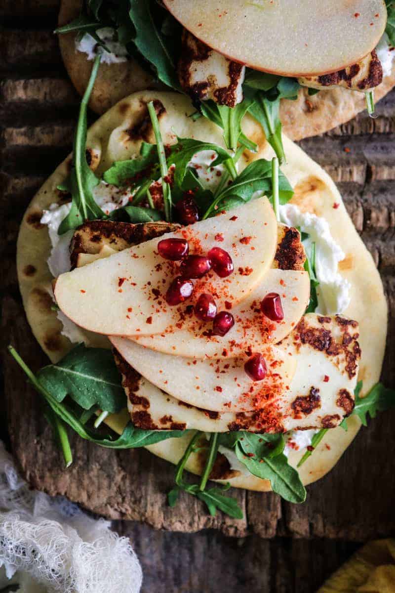 flatbread topped with labneh, arugula, pan seared halloumi, apple, pomegranate, aleppo pepper