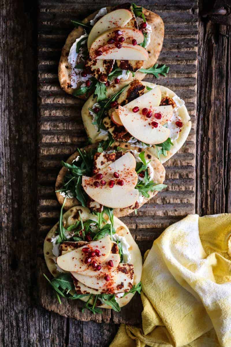 flatbread topped with labneh, arugula, pan seared halloumi, apple, pomegranate, aleppo pepper