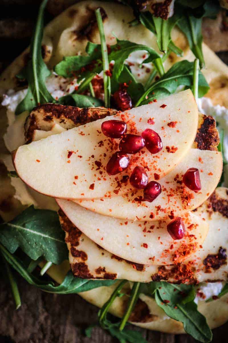 naan layered with labneh, arugula, halloumi cheese, thinly sliced apples, pomegranate, and aleppo pepper