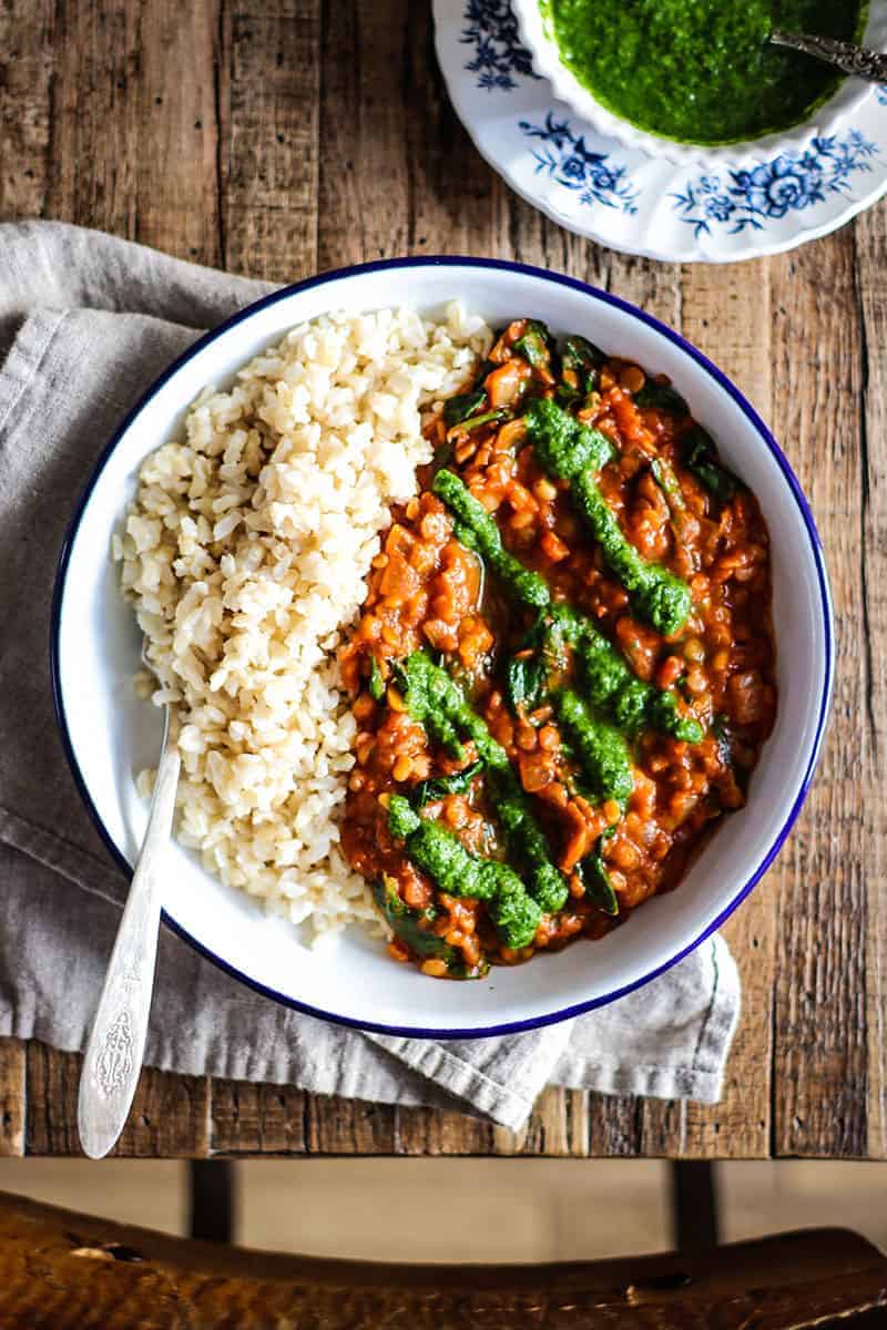 bowl of brown rice with red lentil coconut curry and drizzled with green cilantro chutney