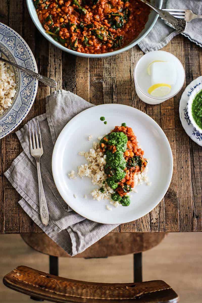 Plate pf brown rice topped with red lentil coconut curry and cilantro chutney