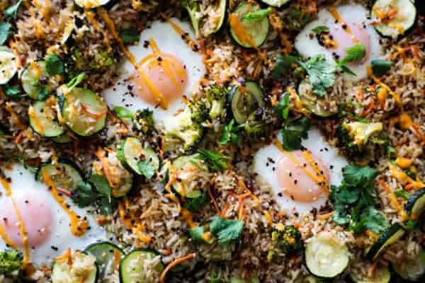 fried rice on a sheet pan with carrots, zucchini, sunny side up eggs and herbs