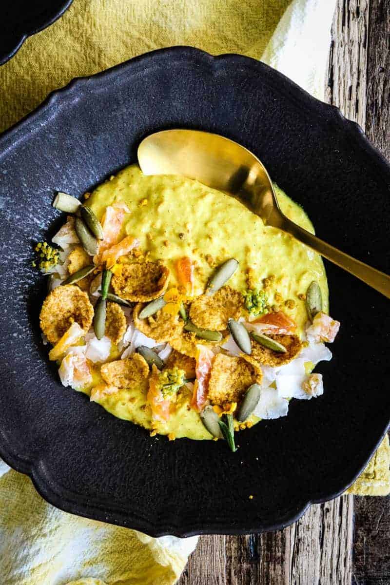 a bowl of yellow golden milk yogurt topped with granola, dried mandarins, pepitas, and coconut