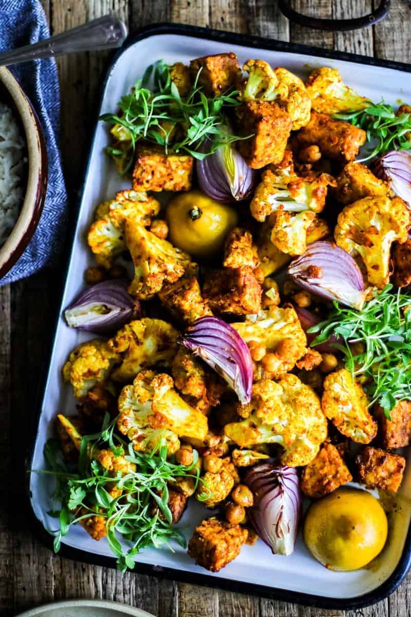 marinated chunks of tempeh, on a sheet pan with roasted cauliflower, chickpeas, onion wedges, and lemons.