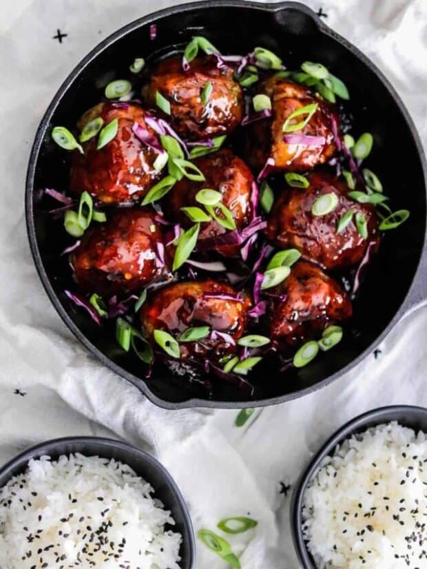Korean BBQ Meatballs in a skillet with green onions and red cabbage. @ bowls of rice on the side with black sesame seeds.