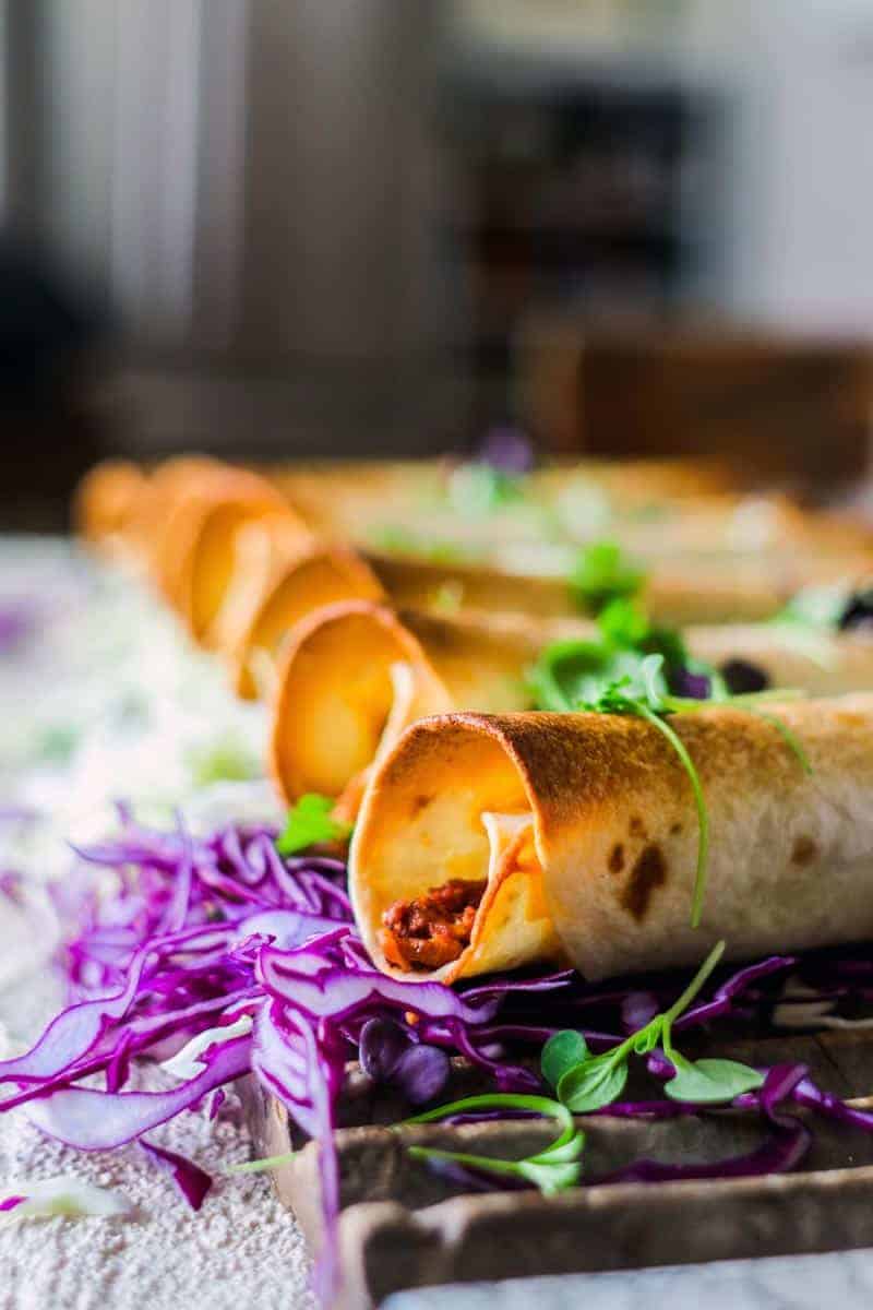 Vegetarian Chili Cheeseburger Taquitos on top of purple cabbage