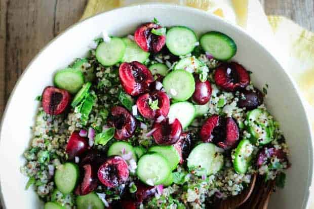 A fresh spin on tabbouleh, Cherry Basil Tabbouleh is in a bowl and is a mix of quinoa, halved cherries, thin slices of cucumber, minced red onion, and basil.