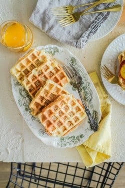 waffles on serving plate and in a stack with sliced peaches on top. Maple syrup and orange juice on the side.