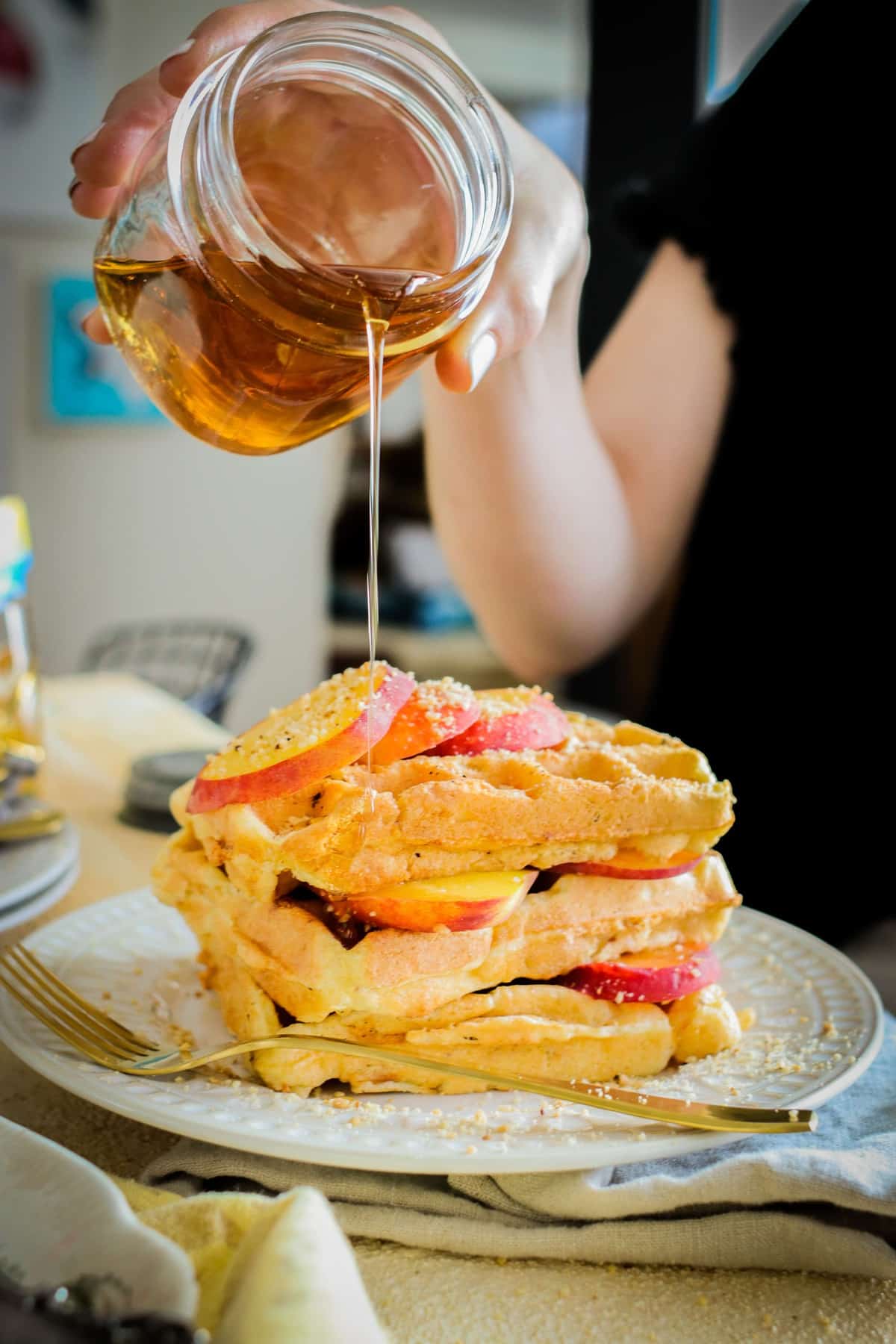 Stack of waffles with sliced peaches being drizzled with maple syrup