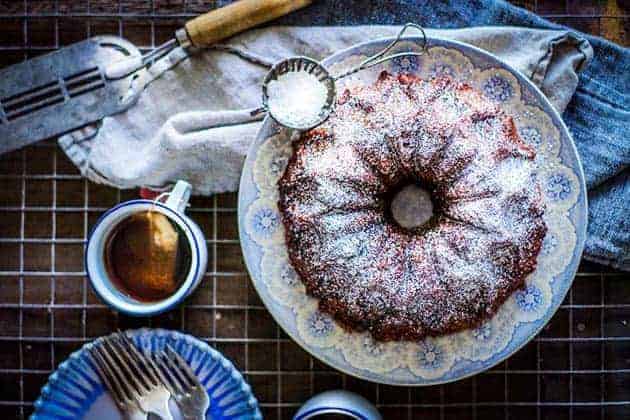 Apple chai monkey bread on a blue and white plate, dusted with powdered sugar. White mugs with a blue rim of chai tea on the side. A linen napkin, blue dessert plate and spatula are also on the table top.