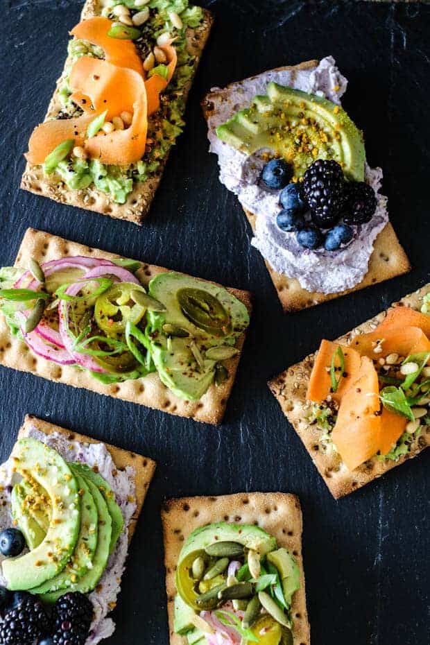 6 various avocado crispbreads with toppings arranged on top of a black slate board