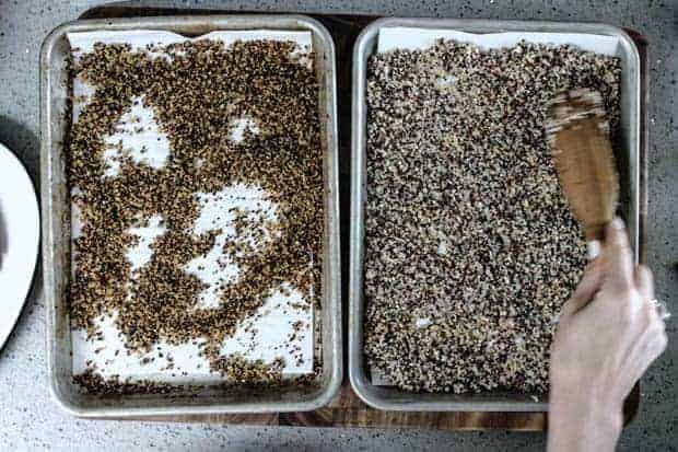 2 baking pans side by side on gray kitchen counter ; one with leftover, cooked tricolor quinoa and one with quinoa after it has baked to a crisp golden brown.