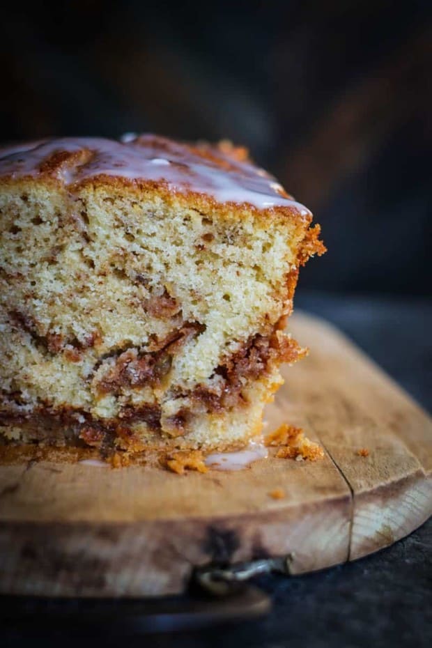 A close up shot of a pound cake. A slice has been cut off so you can see the inside. The loaf cake is a vanilla base with swirls of cinnamon sugar and shredded apples throughout the loaf.