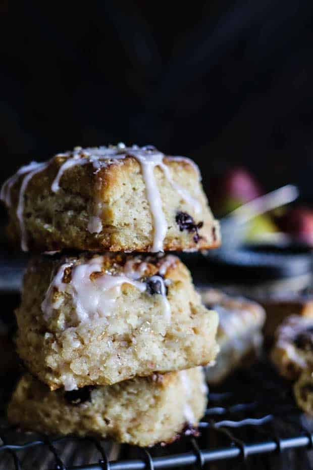 3 dark chocolate pear scones are stacked on top of each other on a wire cooling rack. There is fresh pear icing drilling down the scones and a bowl of red and green pears in the background.